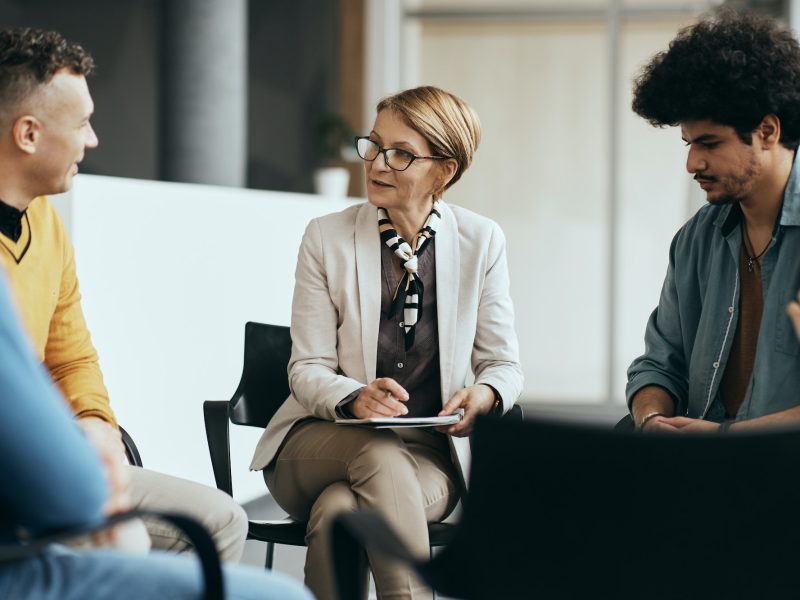 mature-therapist-talking-to-participants-of-group-therapy-at-mental-health-center-.jpg